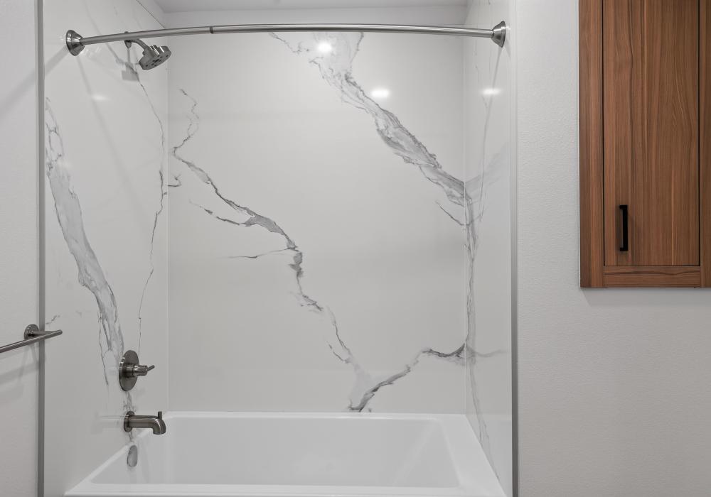 Tub and shower with marble-look surround and wood wall cabinet at The Colton in Redwood City, California