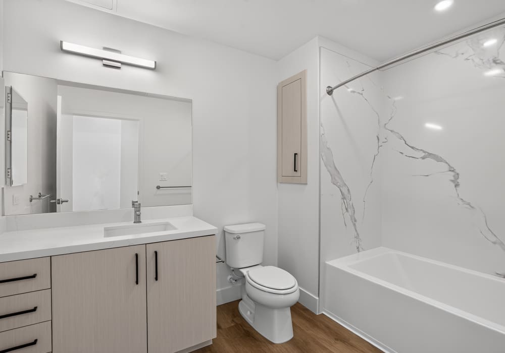 Bathroom with quartz vanity, mirror, toilet and tub with marble walls at The Colton in Redwood City, California