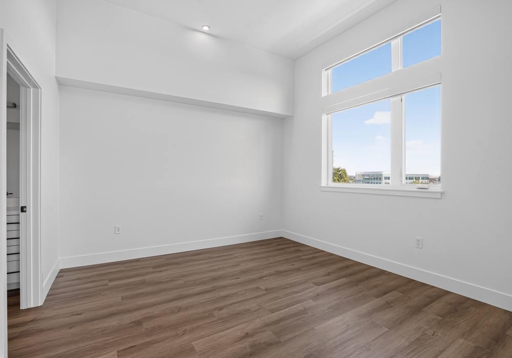 Empty bedroom with tall window, closet doorway and plank flooring at The Colton in Redwood City, California