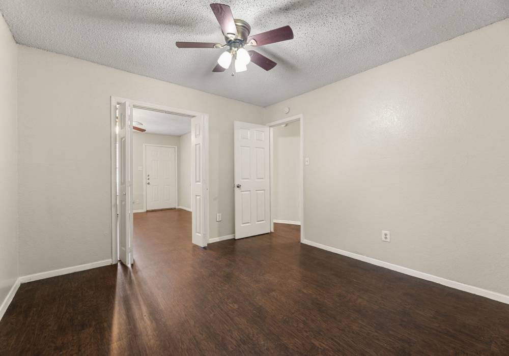Empty bedroom with dark plank flooring, ceiling fan and hallway to entry at Country Oaks in Weatherford, Texas