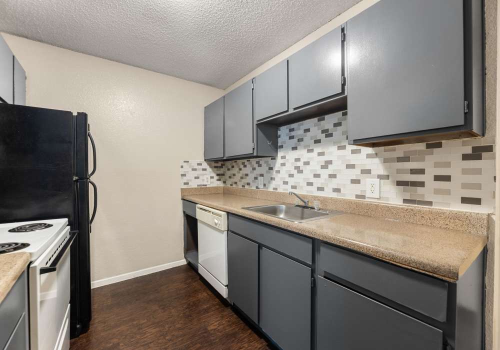 Kitchen with gray cabinets, white dishwasher, tile backsplash and sink at Country Oaks in Weatherford, Texas