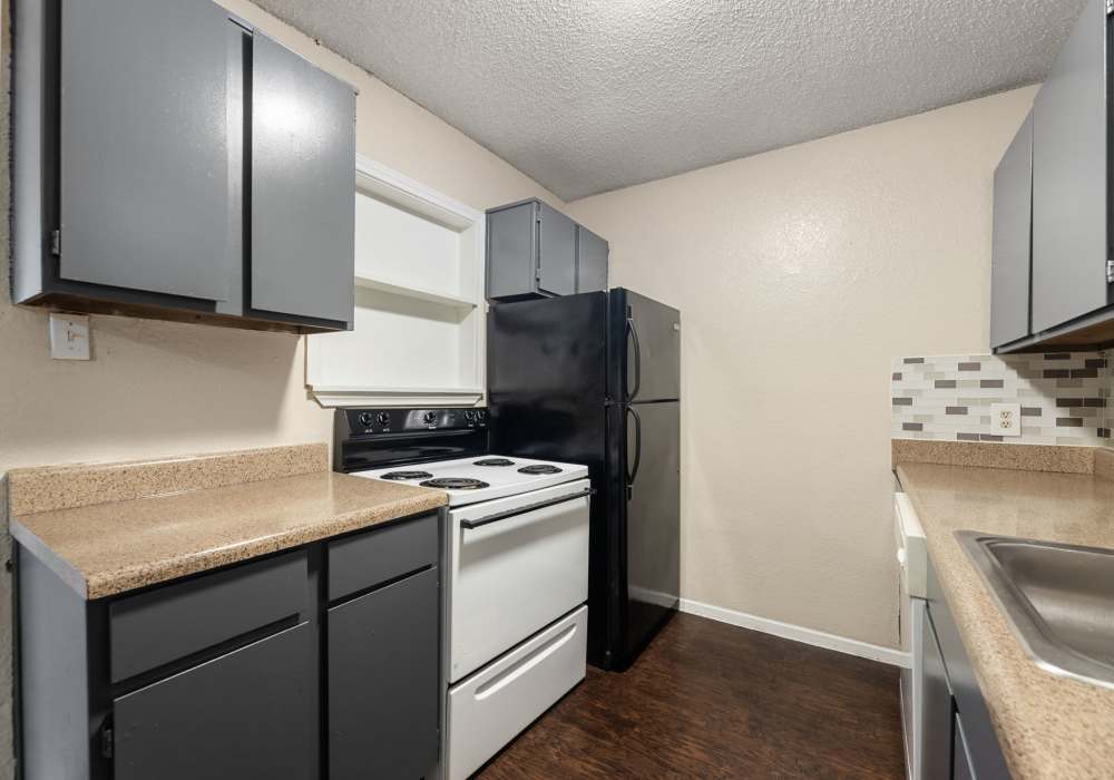 Kitchen corner with gray cabinets, black refrigerator, white range and tile backsplash at Country Oaks in Weatherford, Texas