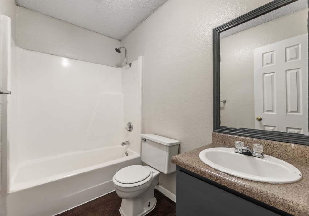 Bathroom with tub, toilet and dark vanity beneath a black-framed mirror at Country Oaks in Weatherford, Texas