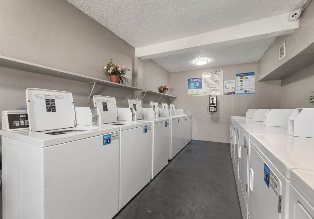 Laundry room with a row of top-load washers, wall shelf and payphone-style card reader at Country Oaks in Weatherford, Texas