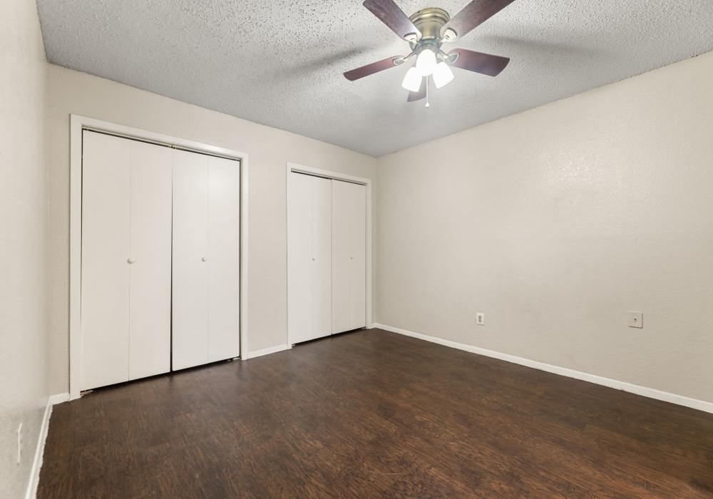 Empty bedroom with two double-door closets, ceiling fan and dark plank flooring at Country Oaks in Weatherford, Texas