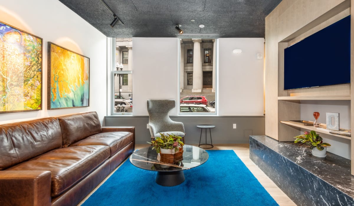 Community lounge with leather sofa and large area rug at One India Street Apartments in Boston, Massachusetts