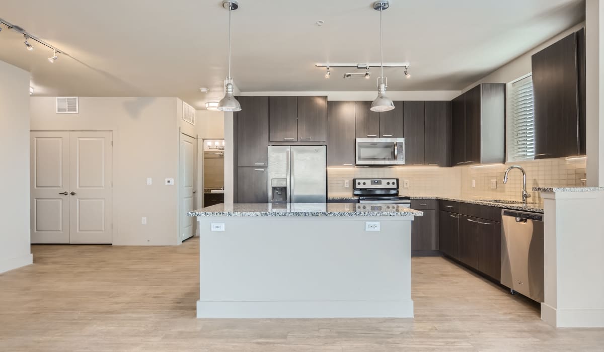 Open-layout kitchen and living room separated by island with waterfall faucet sink and dishwasher at The Lucas Apartments in Dallas, Texas