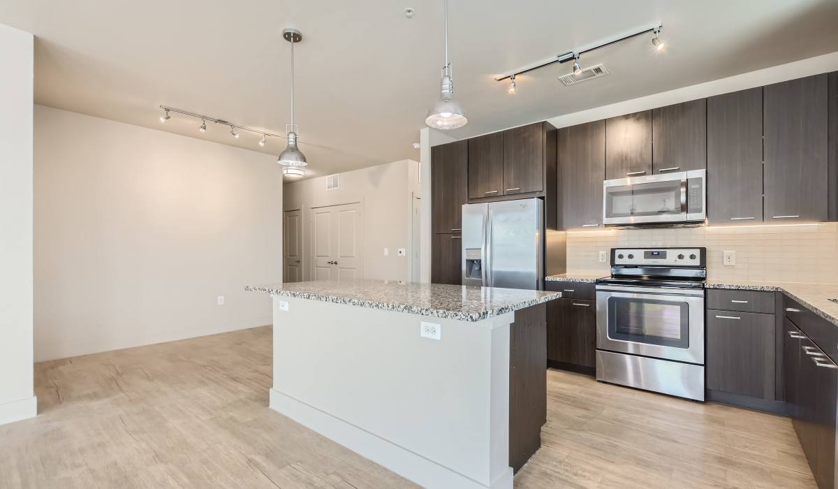 A contemporary kitchen with sleek stainless steel appliances, rich wood floors, and oak cabinets at The Lucas Apartments in Dallas, Texas