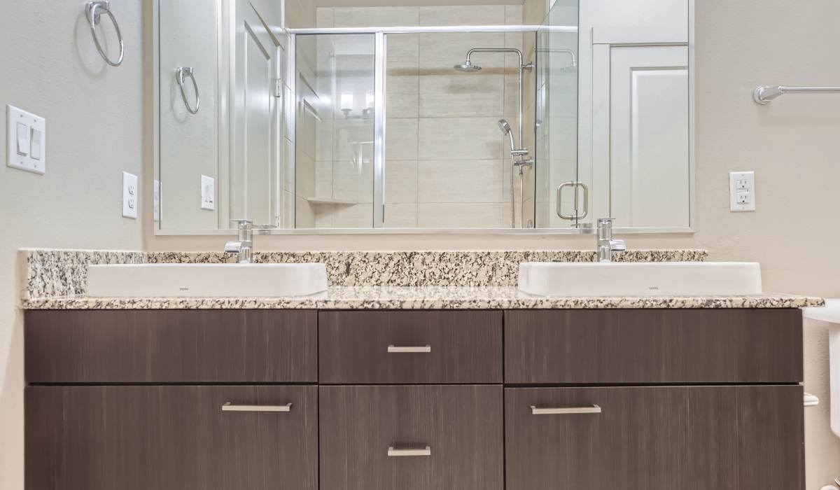 Bright bathroom with vanity lights, cabinets, large mirror and a commode at The Lucas Apartments in Dallas,Texas