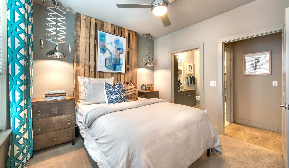 A king-sized bed in an apartment bedroom with a ceiling fan and window at The Lucas Apartments in Dallas, Texas