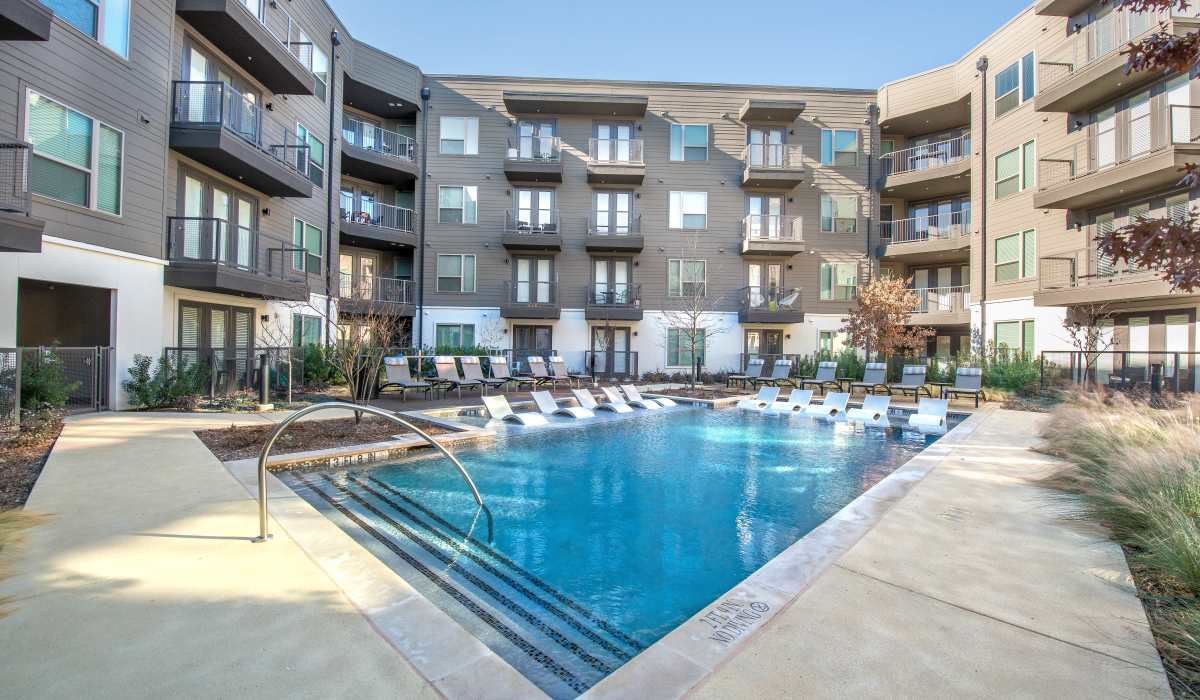 Sparkling swimming pool with lounge chairs and access to clubhouse at The Lucas Apartments in Dallas, Texas