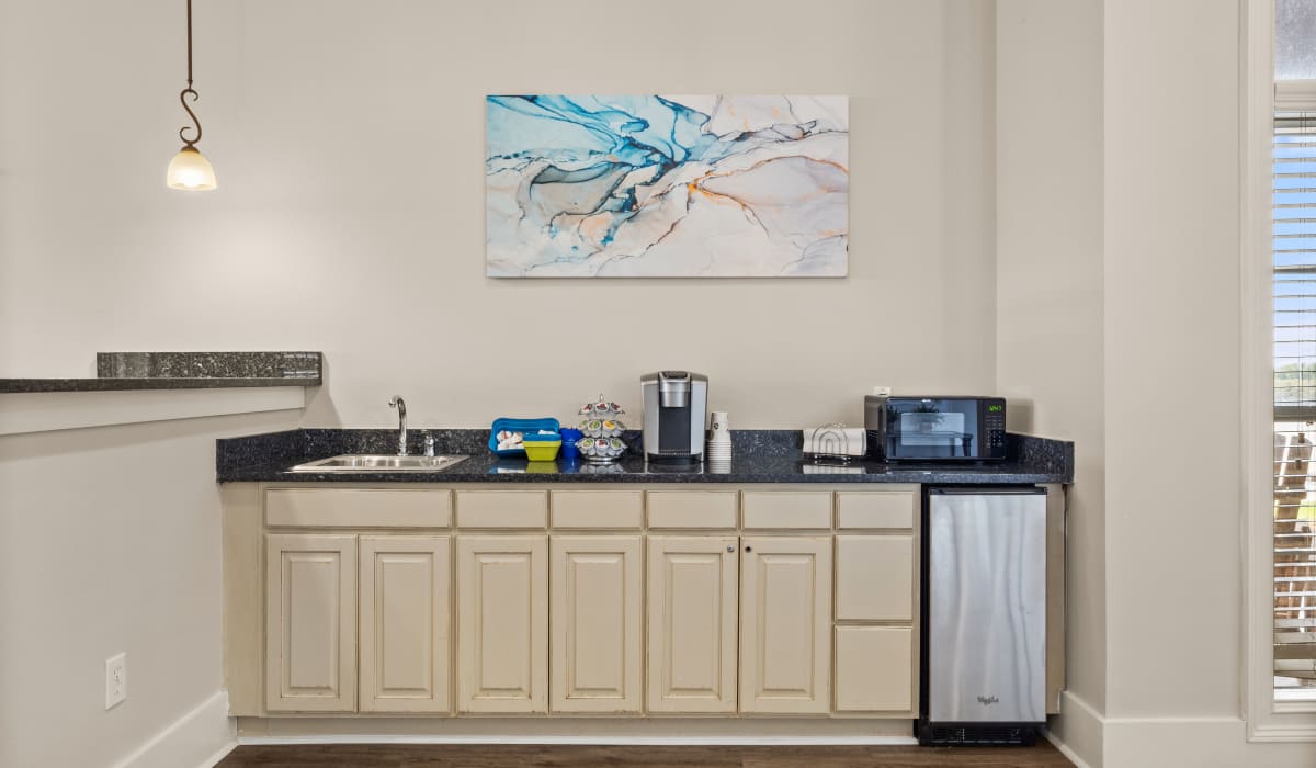 Community kitchen with a coffee machine, granite countertop and wooden storage units at Ansley Place in Houma, Louisiana