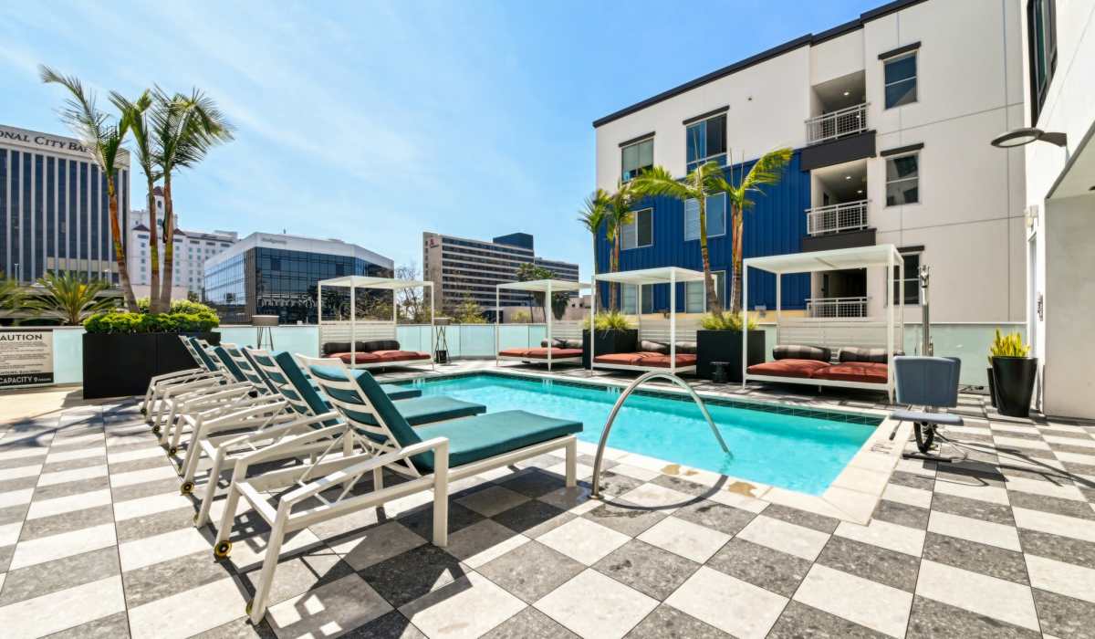 Swimming pool with beach chairs and small palm trees at Aster in Long Beach, California
