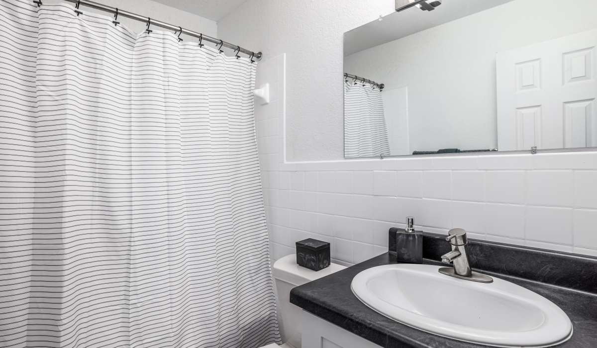 Bright bathroom with a white shower curtain, modern sink, and sleek black countertop at Altitude 405 in Oklahoma City, Oklahoma