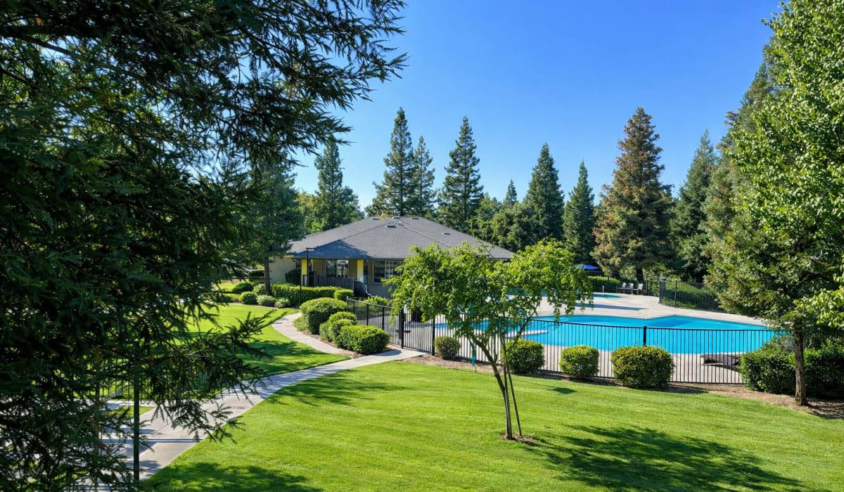 Swimming pool with clubhouse surrounded by trees and green landscaping at Coventry Cove in Clovis, California