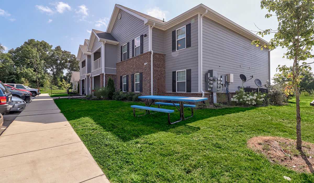 Apartment community with green lawn, picnic table, and parking area near the building at Oliver Crossing in Linden, Tennessee