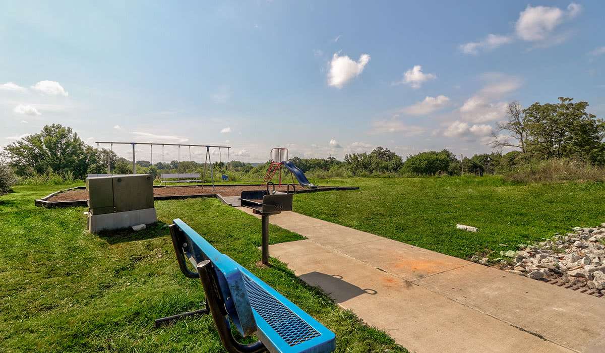 Playground area with swings and slide, grassy space, picnic bench, and clear blue sky at Oliver Crossing in Linden, Tennessee