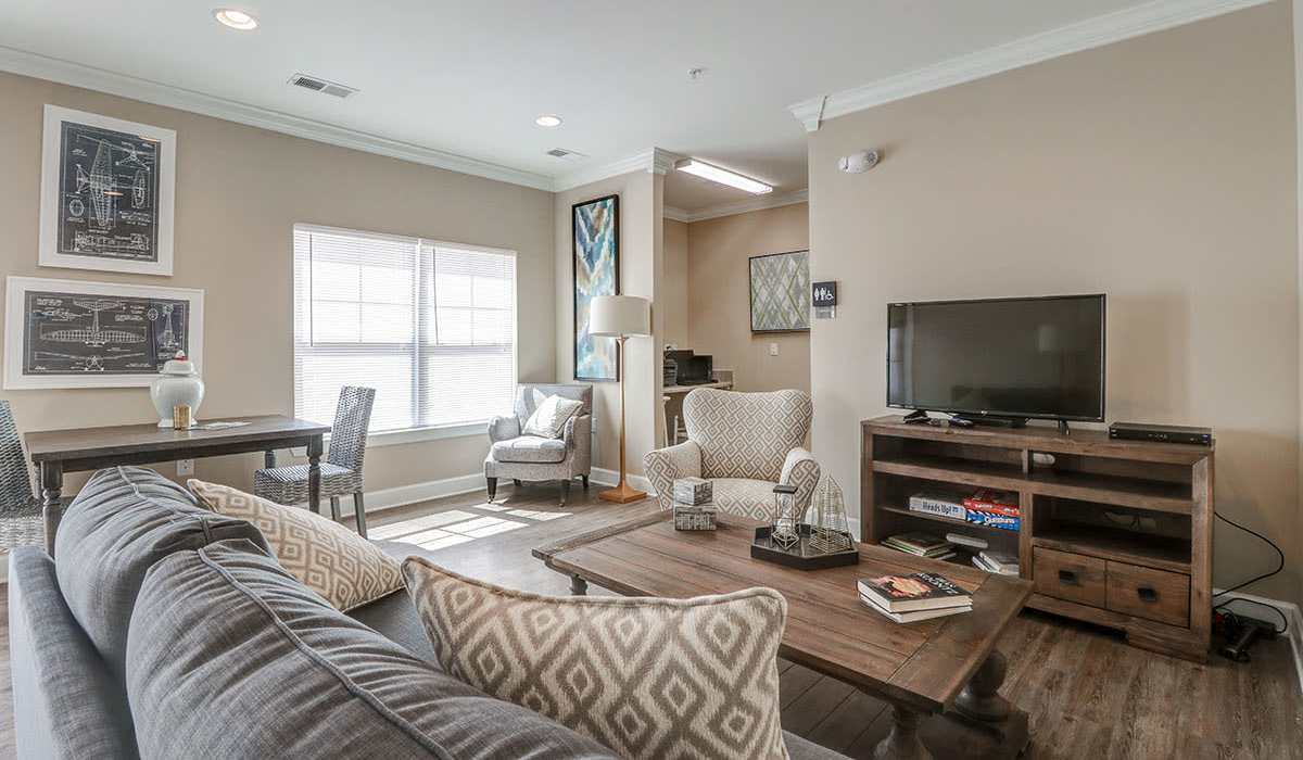 Bright living room with wood-style flooring, cozy seating, and natural light from large windows at Oliver Crossing in Linden, Tennessee