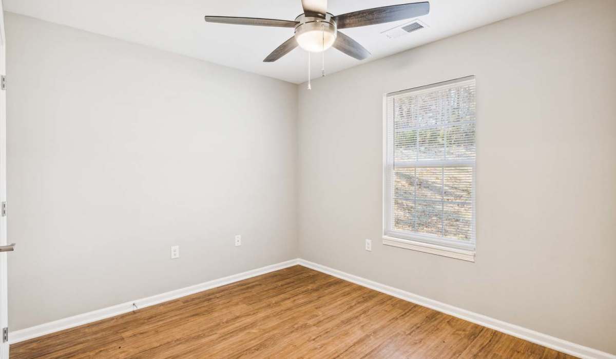 Bright bedroom with wood-style flooring and ceiling fan, large window with blinds at Woodbury Crossing in Corryton, Tennessee