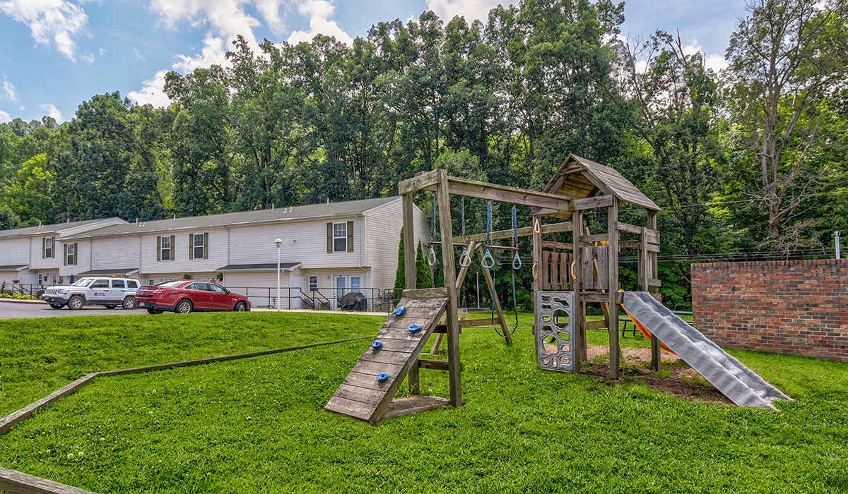 Playground with climbing structure and slide surrounded by green grass and trees in the background at Oakmont Greene II in Mount Hope, West Virginia