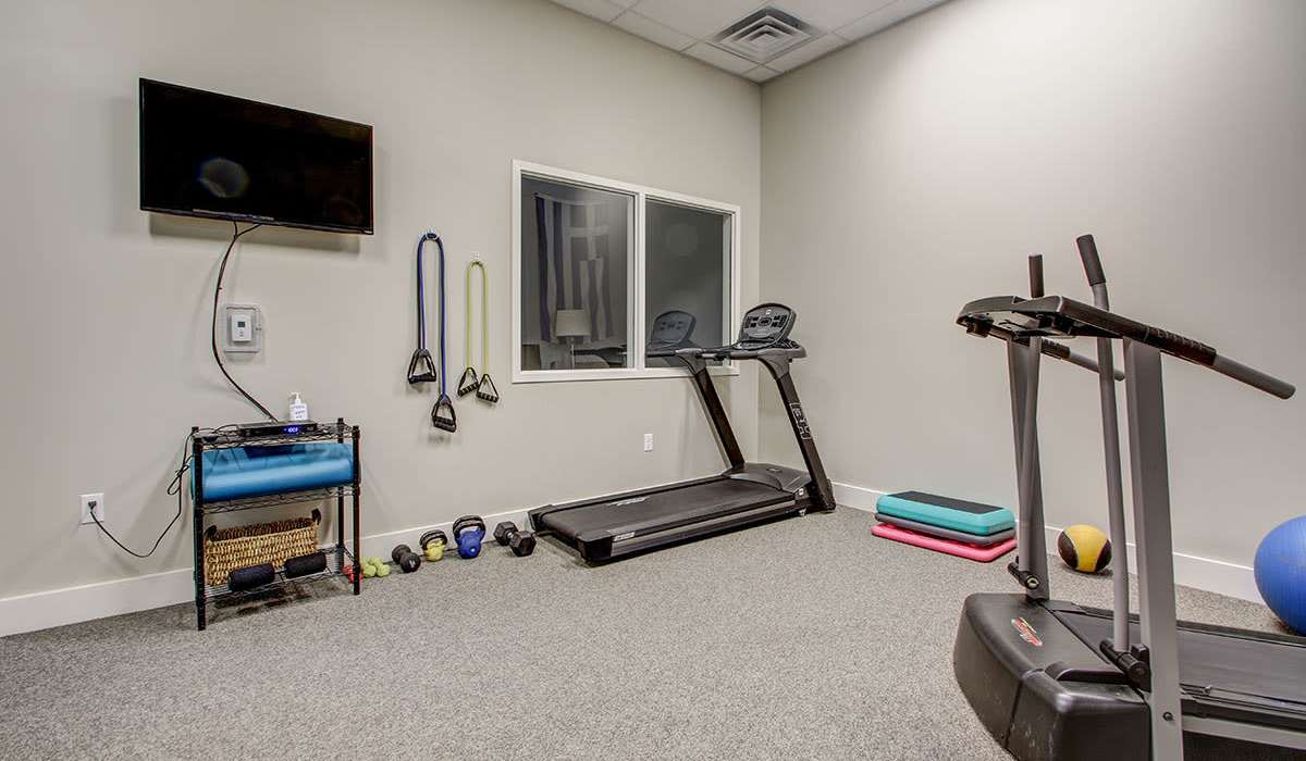 Fitness room with treadmill, weights, exercise mats, and wall-mounted TV at Lloyd House I in Menominee, Michigan