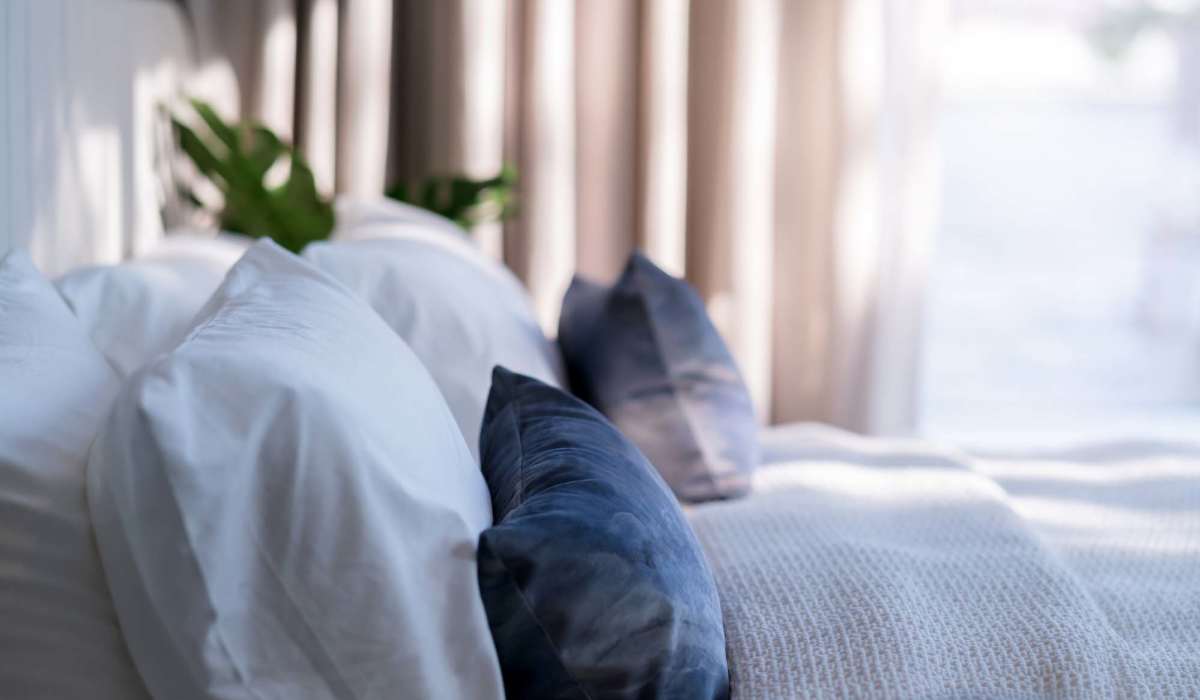 Cozy bedroom with white and blue pillows, soft bedding, and natural light from large windows at Shea Ravines in Wyoming, Michigan