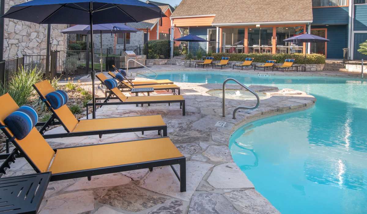 Outdoor pool with yellow lounge chairs and blue umbrellas at The Lila at Oakgate in San Antonio, Texas