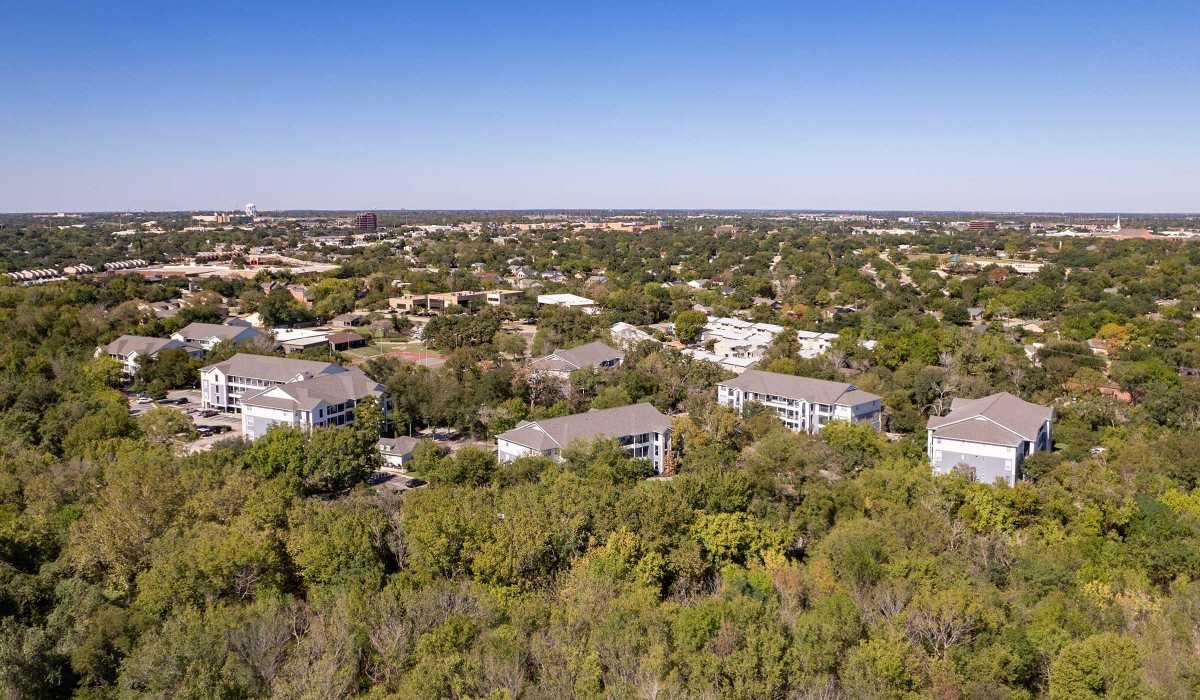 Upgraded aerial view of apartment buildings surrounded by trees at The Element in Bryan, Texas
