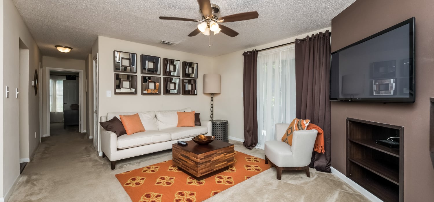 Expansive model living area with wall-to-wall carpeting, a ceiling fan, and built-in console shelving at Tuscany Pointe at Tampa Apartment Homes in Tampa, Florida