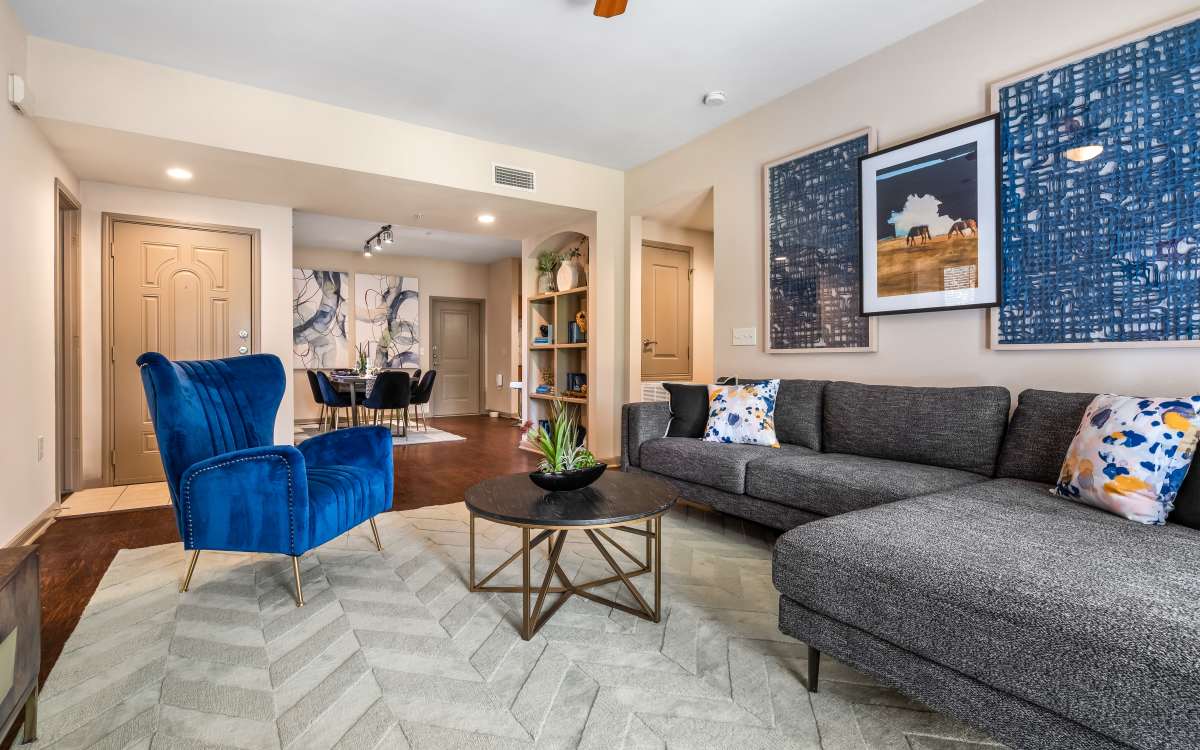 A living room with a blue velvet armchair, a gray sofa, and built-in bookshelves at San Cierra in Houston, Texas