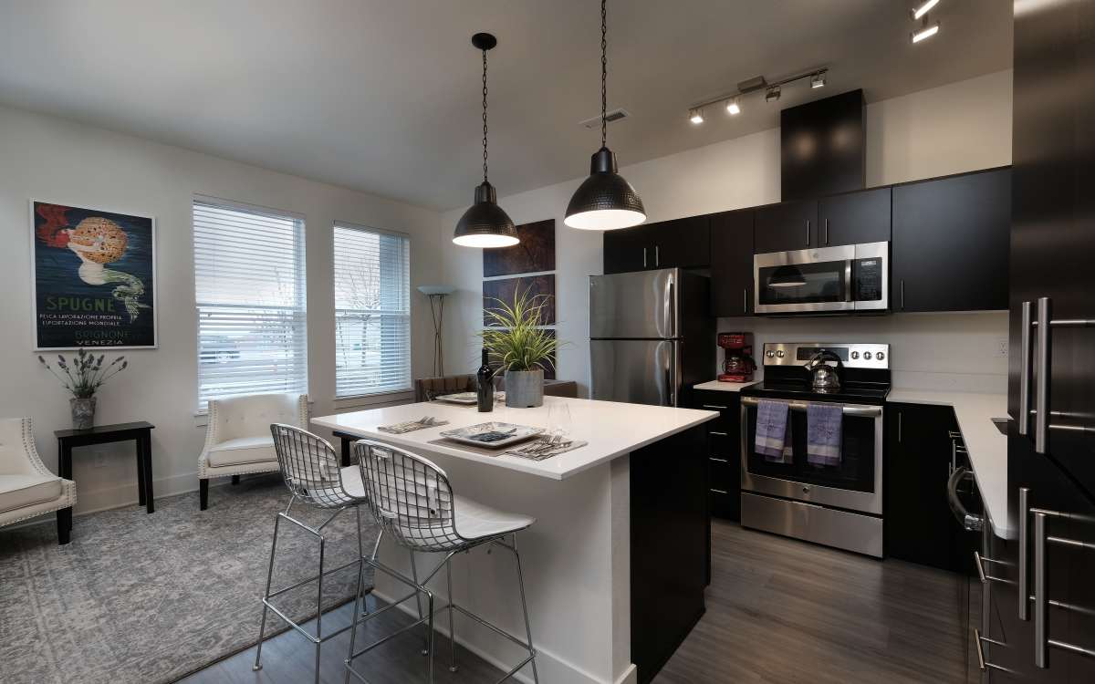 Open-layout kitchen and living room separated by island with waterfall faucet sink and dishwasher at 27 Elm in Redmond, Oregon