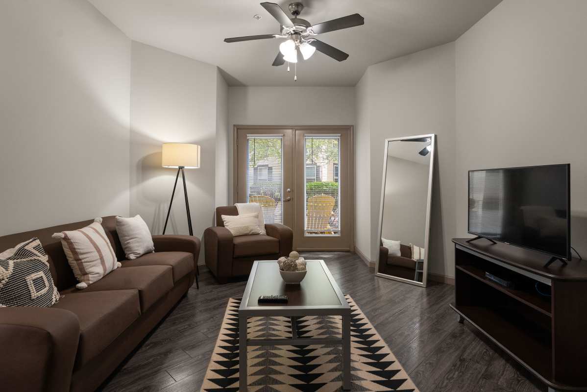 Living room with brown sofa and armchair, floor mirror and mounted TV at The Den in Columbia, Missouri