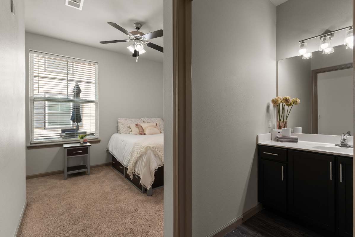 Bedroom and bathroom viewed through doorway with bed, vanity and mirror at The Den in Columbia, Missouri
