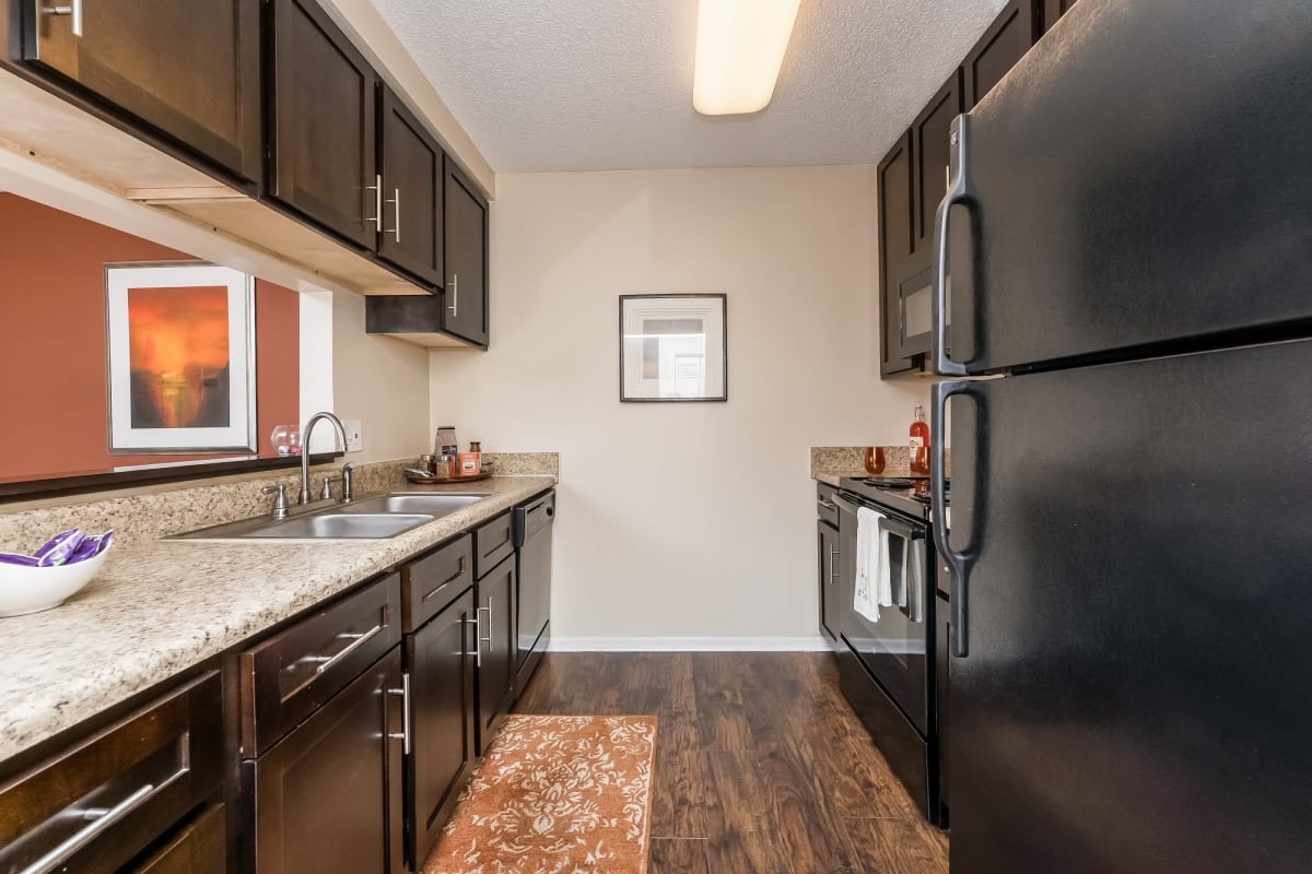 Fully equipped kitchen with sleek black appliances and wood-style flooring at Tuscany Pointe at Tampa Apartment Homes in Tampa, Florida