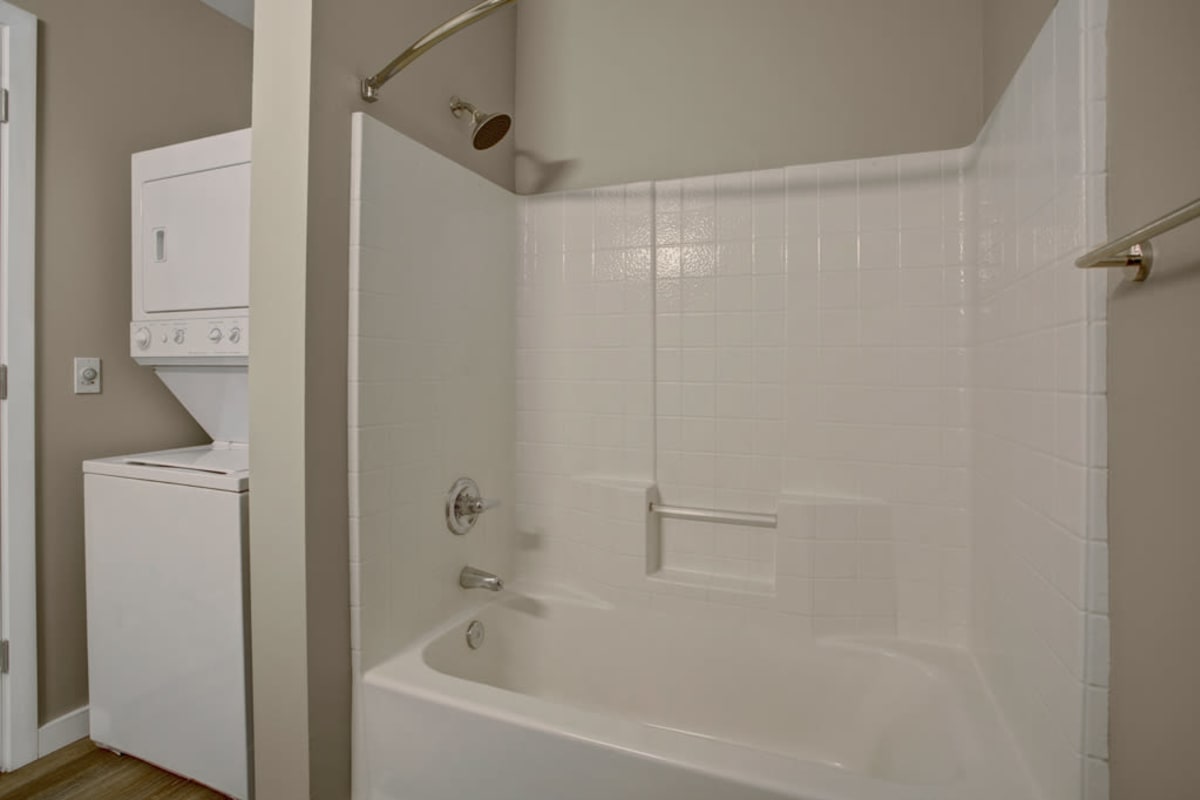 Model home's bathroom with a stacked washer and dryer adjacent to the bathtub and shower at 700 Broadway in Seattle, Washington
