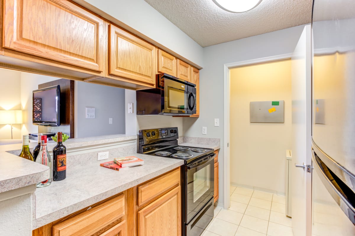 Fully equipped kitchen with black appliances and pass-through window to the living room of a model home at The Lakes of Schaumburg Apartment Homes in Schaumburg, Illinois