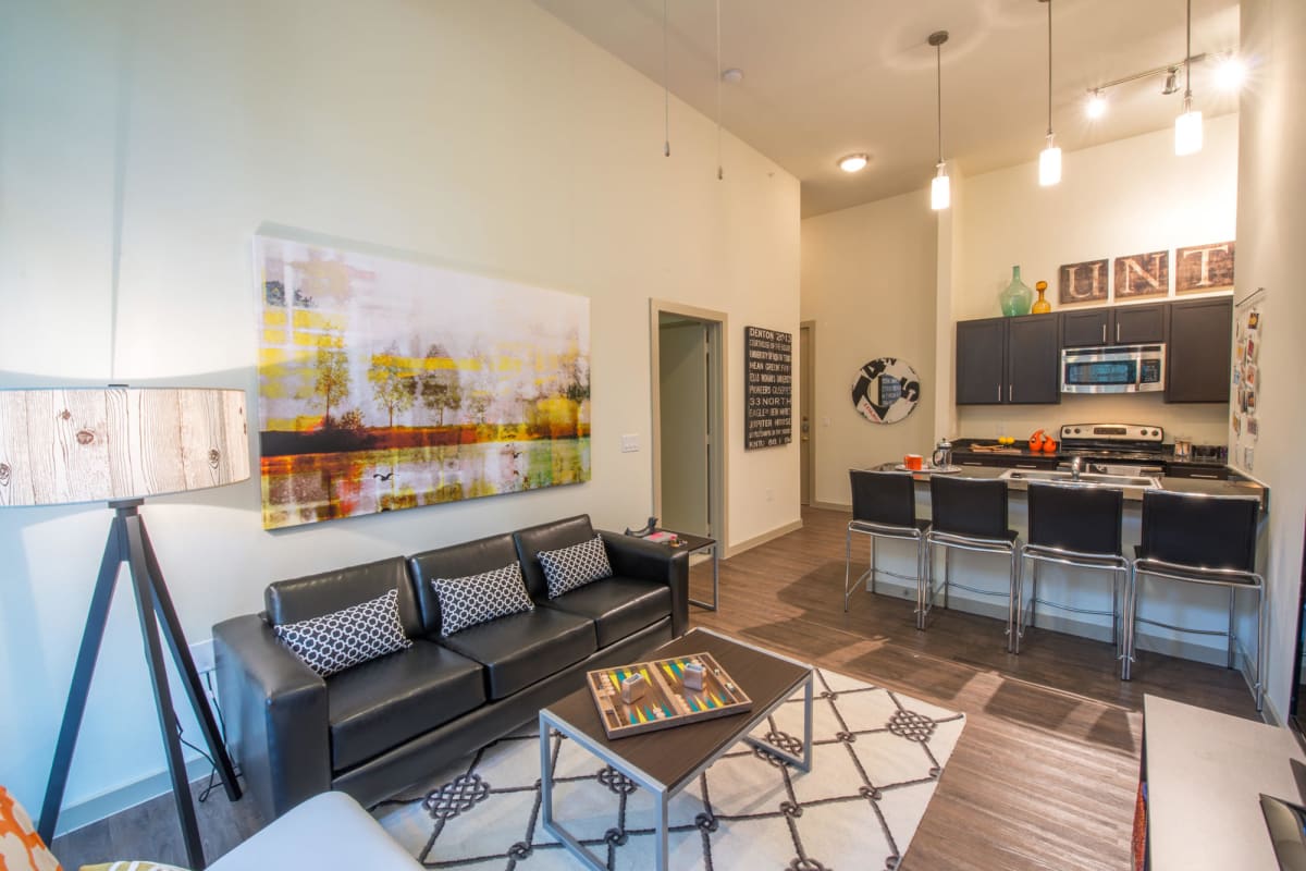 Modern furnishings and custom wood cabinetry in a model student apartment's open-concept living and kitchen areas at 33 North in Denton, Texas