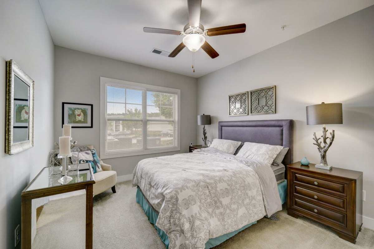 A cozy gray painted bedroom with bedside cabinets and lamps and a ceiling fan at Century Park Place in Morrisville, North Carolina