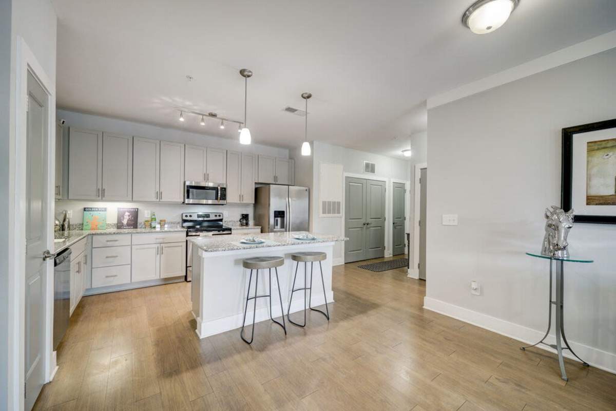 A room showcasing the kitchen area with a kitchen island bar with two high chairs and multiple modern appliances at Century Park Place in Morrisville, North Carolina