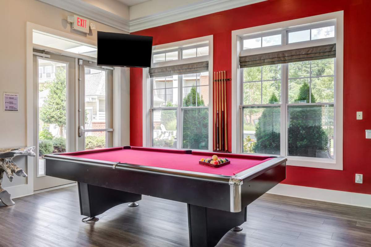 A pool table in a room with red walls, featuring a television mounted on the wall at Century Park Place in Morrisville, North Carolina