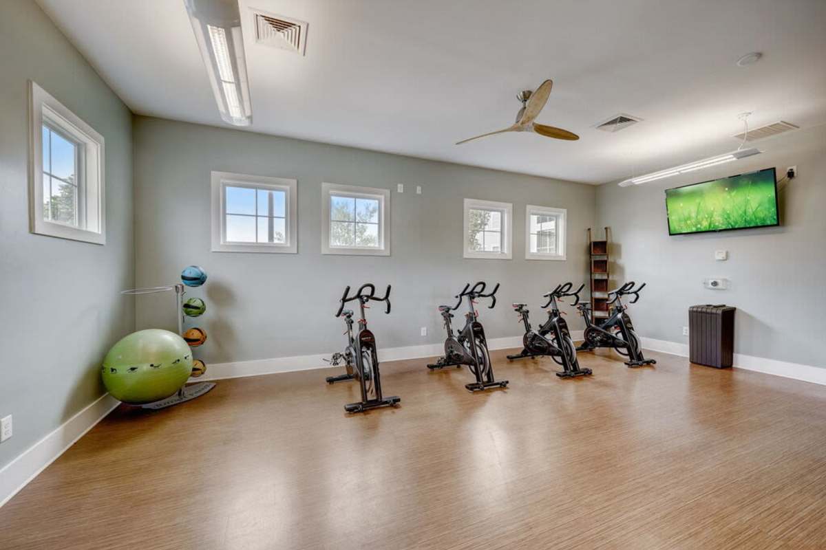 A gym room featuring several exercise bikes and a wall-mounted television for entertainment during workouts at Century Park Place in Morrisville, North Carolina