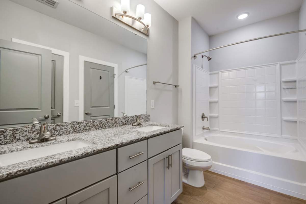 An empty bathroom with two sinks and a huge mirror with toilet bowl and a bathtub at Century Park Place in Morrisville, North Carolina