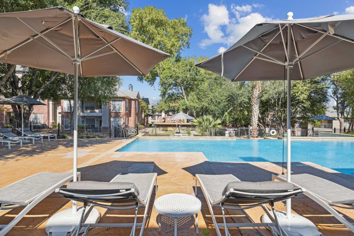 Beach Chairs With Umbrellas Beside A Swimming Pool at Whispering Creek Villas, San Antonio, Texas