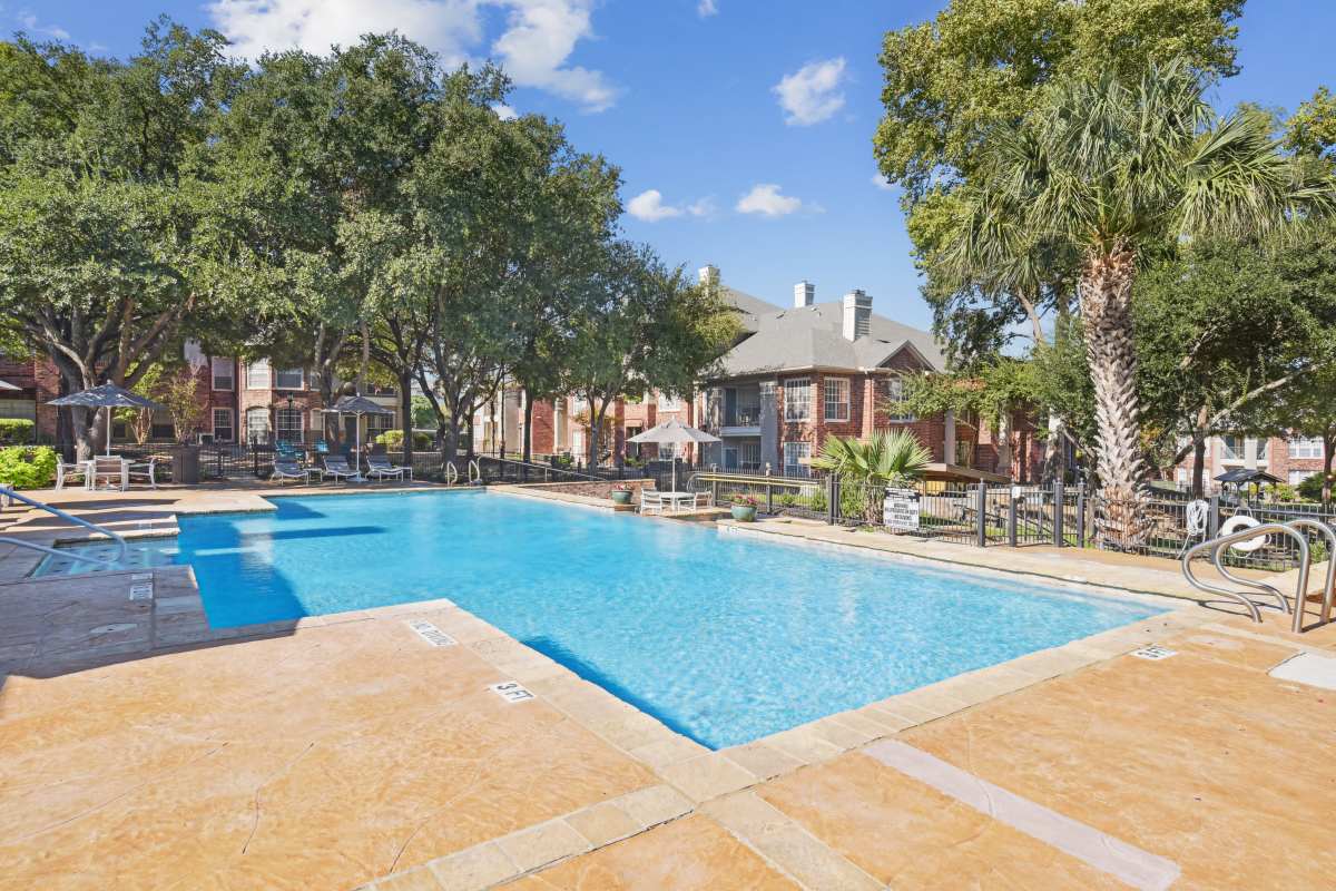 Bright Blue Swimming Pool Surrounded By Trees And Buildings at Whispering Creek Villas, San Antonio, Texas
