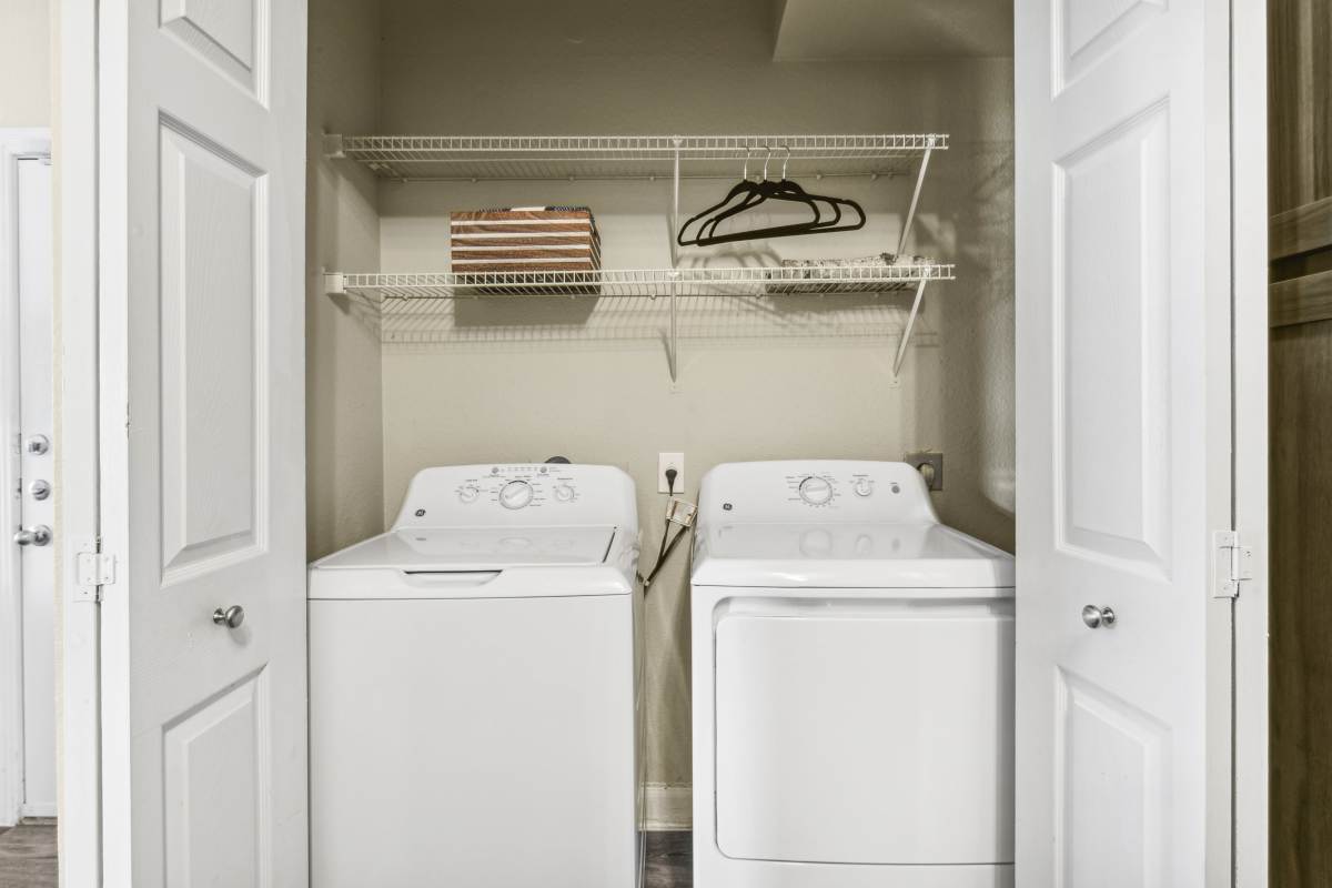 Laundry Closet With A Washer And Dryer And Wire Shelving at Whispering Creek Villas, San Antonio, Texas