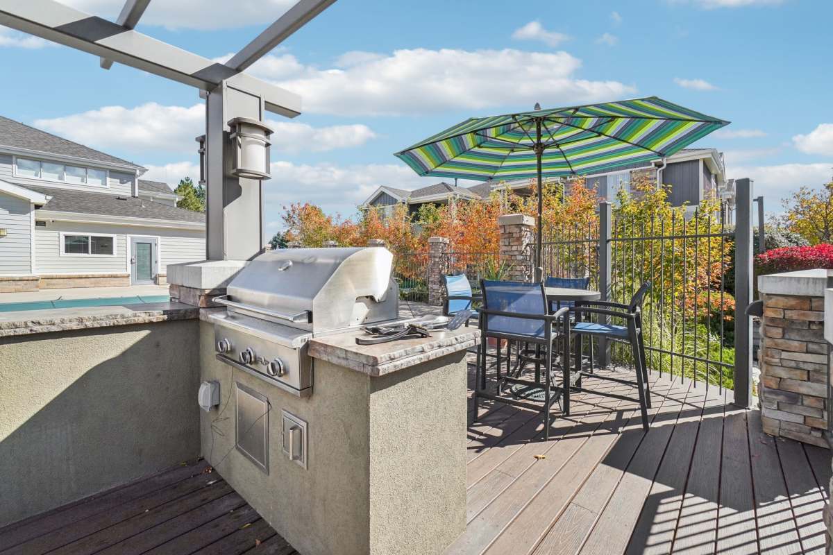 Outdoor patio with built-in grill, dining table, and striped umbrella, surrounded by autumn trees and a residential backdrop at Pavilions at Silver Sage in Fort Collins, Colorado.