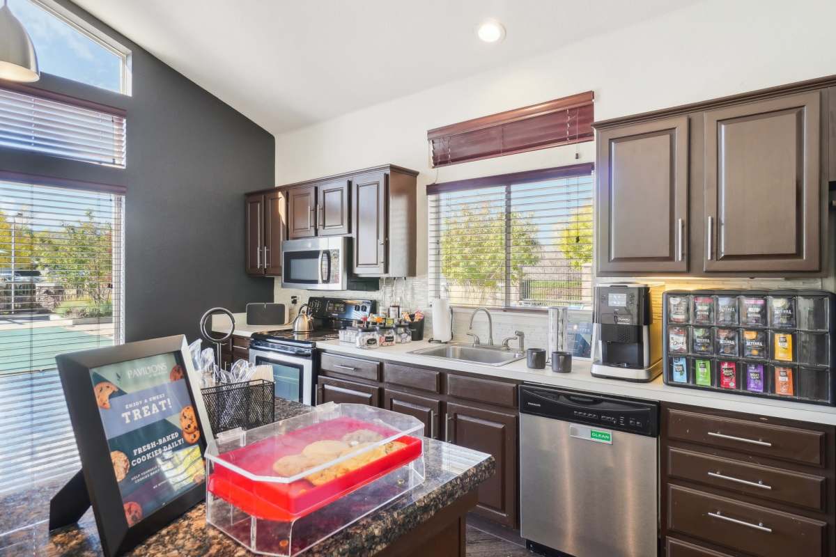 Modern kitchen with dark cabinets, stainless steel appliances, granite countertops, and a cookie station with a coffee machine at Pavilions at Silver Sage in Fort Collins, Colorado.