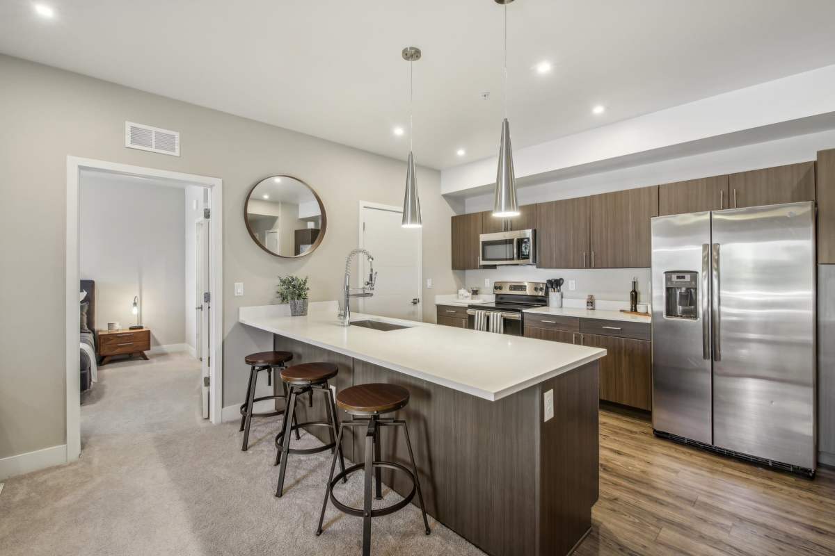 Modern kitchen featuring a large island with bar stools, sleek cabinetry, and stylish lighting fixtures, at The Wyatt Apartments in Fort Collins, Colorado.