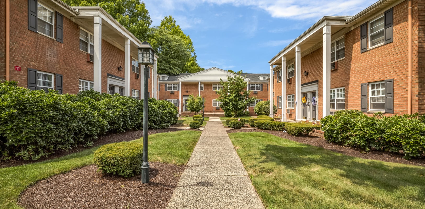 Open walkway with a great lawn on each side between two buildings at Park Lane Apartments in Little Falls, New Jersey