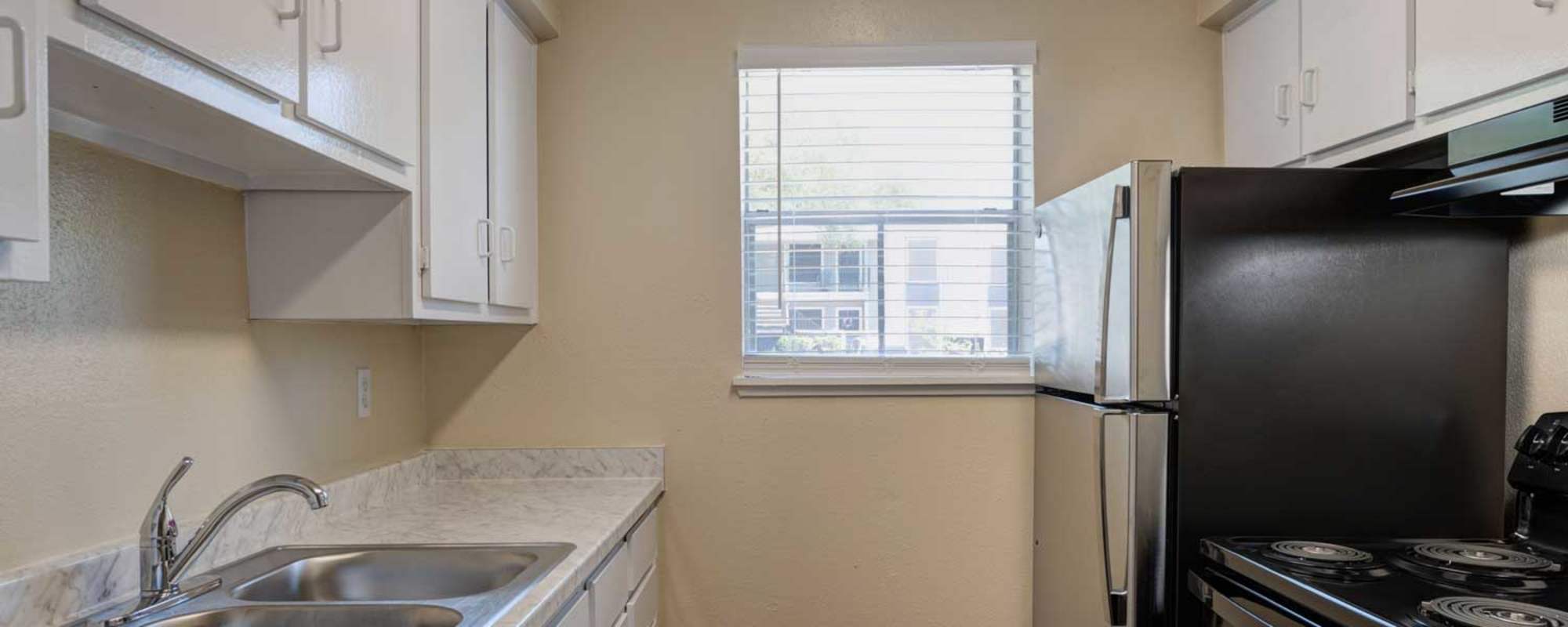 Apartment kitchen with white cabinets and stainless-steel sink at Meyerland Court in Houston, Texas